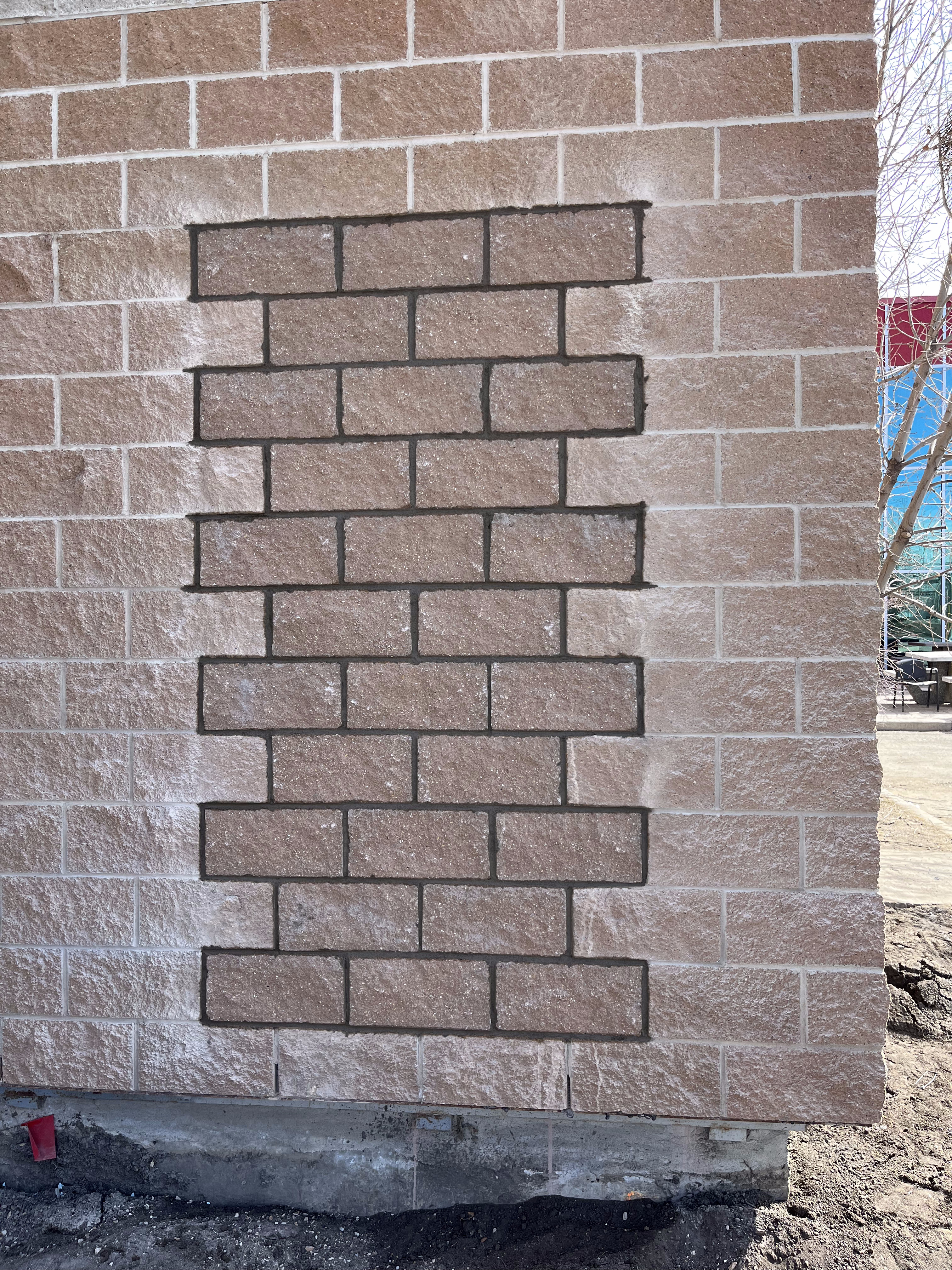 Rock-faced block wall with red brick patch infill repair