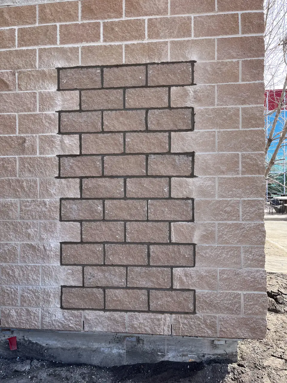 Rock-faced block wall with red brick patch infill repair